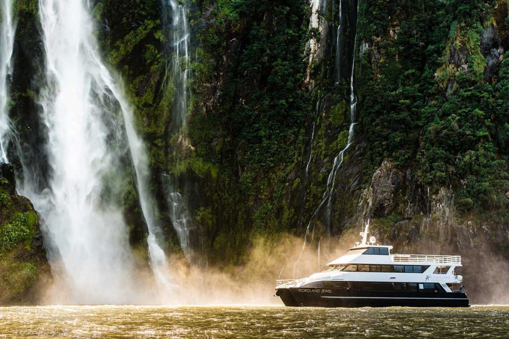 fiordland jewel boat by a waterfall at Milford sound on a luxury day tour with alpine luxury tours